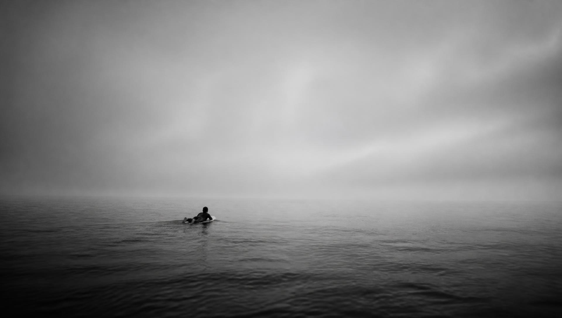 Surfista solitario remando en un mar calmo y neblinoso